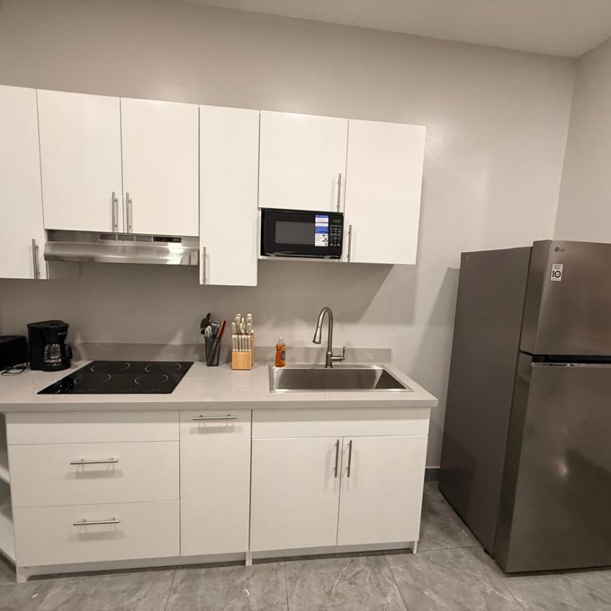 Honeycreeper Suite kitchenette with white cabinets, cooktop, microwave and refrigerator